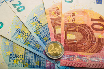 paper euro banknotes and coins. The coin is two euros.