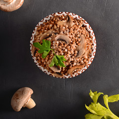 Cooked buckwheat with mushrooms with celery top view on black background