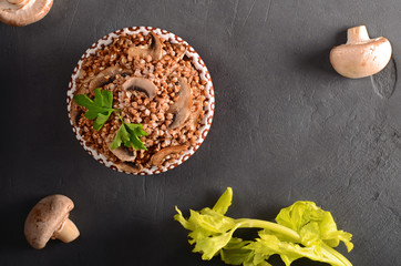 Cooked buckwheat with mushrooms with celery top view on black background