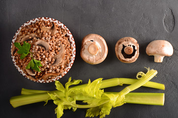 Cooked buckwheat with mushrooms with celery top view on black background