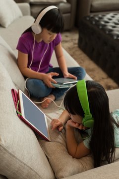 Siblings with headphones using digital tablet while sitting at home