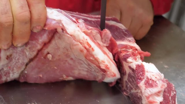 Butcher cuts beef meat in a slaughterhouse with electric saw, top view