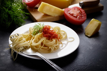 Italian spaghetti on black stone table with pasta ingredients- cheese, tomato and dill