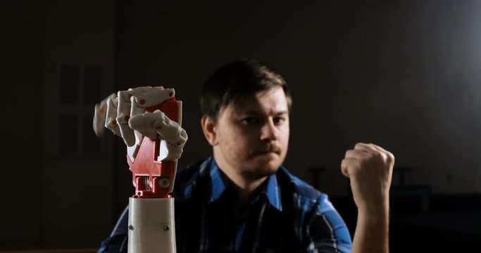 Man creates movement for mechanical plastic arm. Cybernetic robotic arm. Robots arm movement. Futuristic made on 3D printer device.