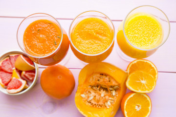 Healthy Food, Diet Concept. Three glasses of fruit and vegetable smoothie in a raw with pieces of fresh orange, pumpkin and grapefruit on pink wooden background, top view