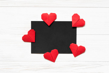 Black paper blank and red origami heart on white wooden background. Mockup for greeting card.