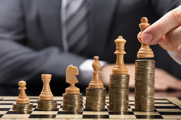Businessperson Placing Chess Pieces On Stacked Coins