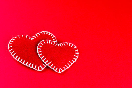 two decorative  hearts made of red fumirana sewn with a white thread, on a red background. Happy Valentine's Day symbol. selective focus. close-up. can be used as a background, copy space