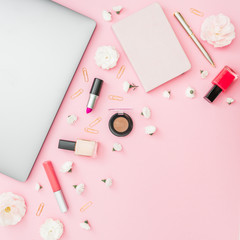 Concept with silver laptop, notebook, cosmetics and flowers on pink background. Top view. Flat lay.