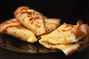 Crepes. Thin pancakes on a dark glass plate on a dark background. Traditional food for Russian carnival.