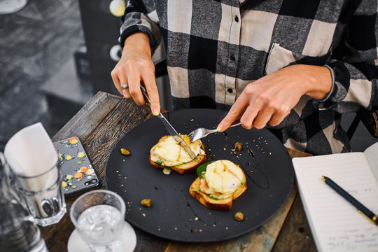 Person eating eggs benedict at a cafe table