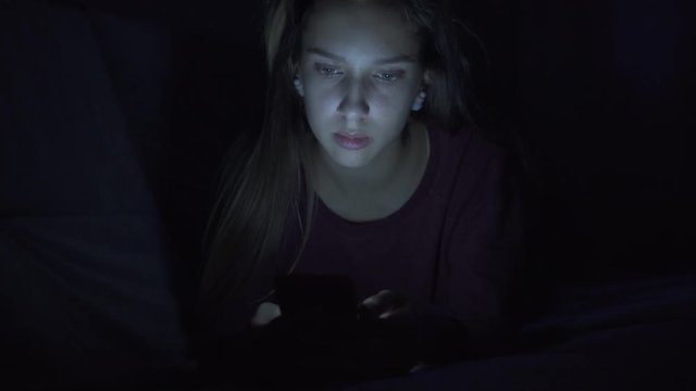 Tired girl texting on mobile phone at night