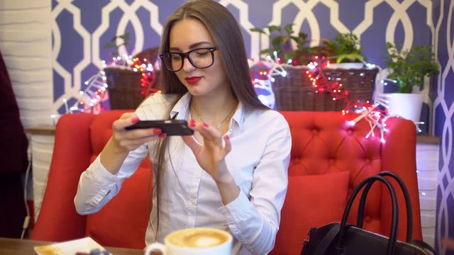 Young business woman taking photo of food with cellphone sitting in cafe. woman photographing food and coffeeby phone. 4 k. Woman taking picture of her breakfast by her smart phone.