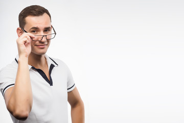 A young positive man in eyeglasses straightens his glasses with his hand. Emotional, courageous face. Isolated on white background. Copy space.