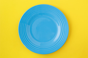 Empty blue plate on yellow. From above view.