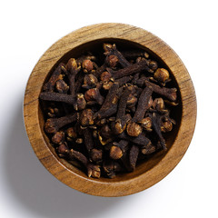 Dry cloves in dark wood bowl isolated on white from above.