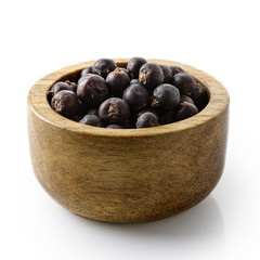 Dry juniper berries in dark wood bowl isolated on white.