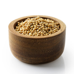 Dry white mustard seeds in dark wood bowl isolated on white.