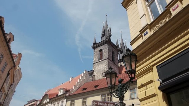 A walking shot down a old town Prague street looking up at the building facades and old cityscape, ancient huge tower, old multistoreyed building with an arc