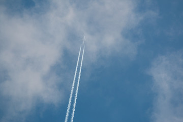 Airplane flying at high altitude leaving its white wake over blue sky