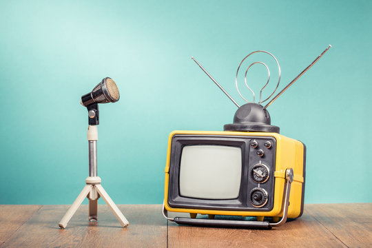 Retro old television receiver and microphone with tripod on table front gradient aquamarine wall background. Broadcasting concept. Vintage style filtered photo