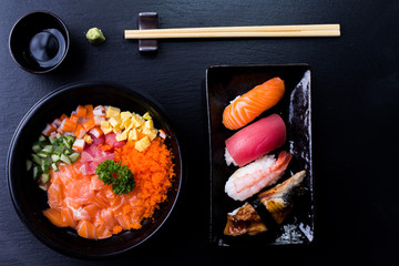 Sashimi sushi and Japanese Tekka Don served on stone slate with dark background.