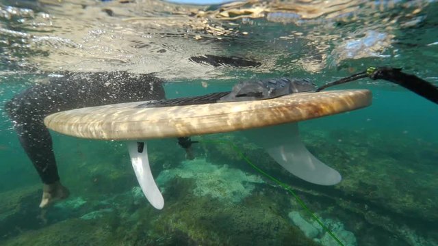Underwater slow motion pro male surfer sitting on surfboard in the clear blue ocean on a sunny day in lobos