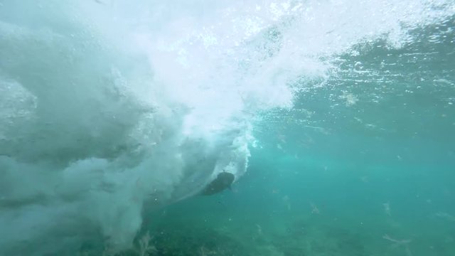 UNDERWATER SLOW MOTION: Unrecognizable pro surfer riding big barrel waves in deep blue ocean in Canary Islands. Thrill seeker surfing on sunlit day. Tube wave rolling into foam and air bubbles.