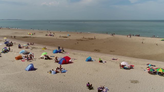 Aerial bird view footage of recreational beach with many people sun bathing and enjoying them on the warm hot sand also showing colorful parasols and beach towels on warm hot summer day 4k quality