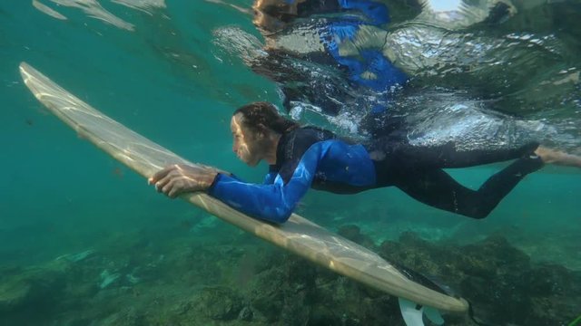 UNDERWATER SLOW MOTION: Extreme surfer laying on his surfboard diving underneath the crystal surface to gain speed. Fit athlete enjoying summer vacation surfing on the Canary Islands. Fun water sports