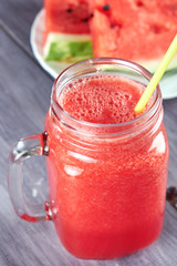 Chopped pieces of watermelon on a white plate and a glass mug with a watermelon smoothie