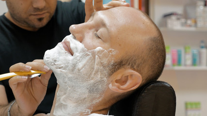 The barber is shaving his client in old fashion manner. Single blade shave gives the best result....