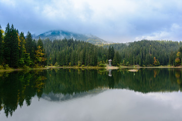 View of Synevir high-altitude lake by autumn day. The leaf fall forest is reflected in water of lake.