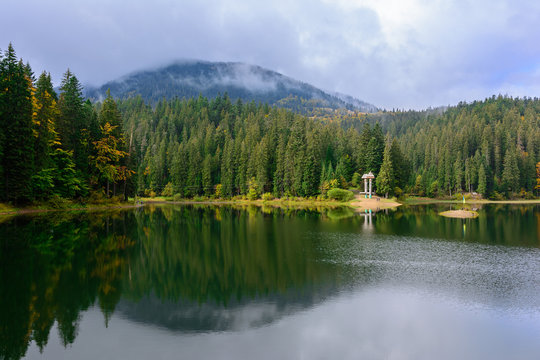 View of Synevir high-altitude lake by autumn day. The leaf fall forest is reflected in water of lake.