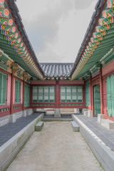 Looking down the middle of a historical building with colorful design and architectural details, in the middle a strip of dirt and the sky above, at Gyeongbokgung Palace, South Korea