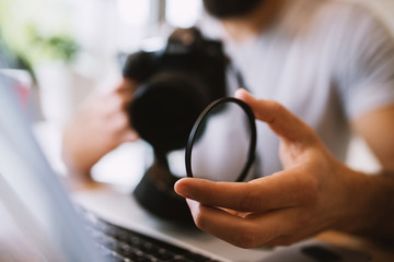 Picture with camera lenses as the most focused and man holding it and a camera in the background.