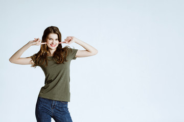 body language and emotions. Studio shot of happy young fair-haired woman  dressed casually jeans and green t-shirt. white background. girl smiles and shows fingers on the teeth.