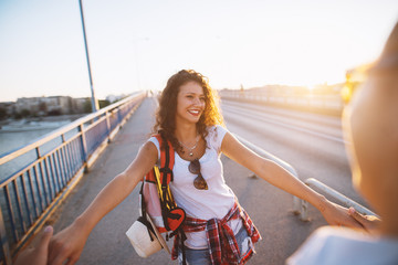 Obraz premium Gorgeous girl with curly hair holding hands with a man while standing on the bridge.