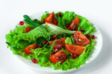 Salad on a white plate on a white background. Cherry tomatoes, arugula and pomegranate seeds on fresh lettuce leaves. Close-up.