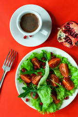  Salad on a white plate, espresso, pomegranate and fork on a red background. Cherry tomatoes, arugula and pomegranate seeds on fresh lettuce leaves.  Flat lay