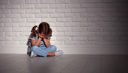 upset sad sad child girl in stress cries at an empty dark wall