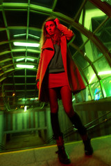 Beautiful young slender woman walks street city underground passage subway light night color gels green red fashionable