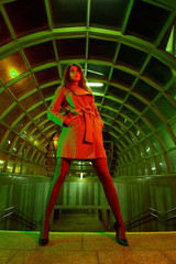 Obraz na płótnie Canvas Beautiful young slender woman walks street city underground passage subway light night color gels green red fashionable