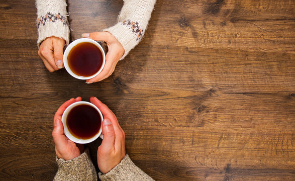 Cups of black tea in the hands of men and women. on a wooden background. with copy space. top view
