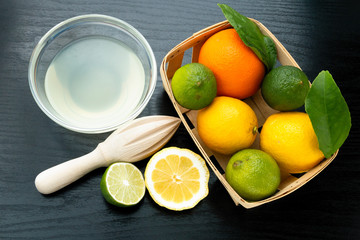 Healthy food and vitamins: a wooden juicer and fresh lemon and lime with leaves and freshly squeezed delicious juice in a glass bowl on a black table