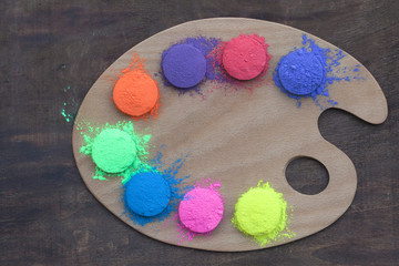 Festival of colors. Bright colors for holi festival. Colorful holi paint (powder) on artist's palette on a table. Close up with copy space. Creative shoot. Natural organic pigment.