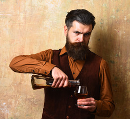 Guy pours cognac into glass from bottle. Man with beard