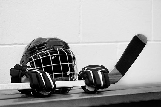 Black and white photo of hockey equipment on the bench: Helmet, gloves and stick