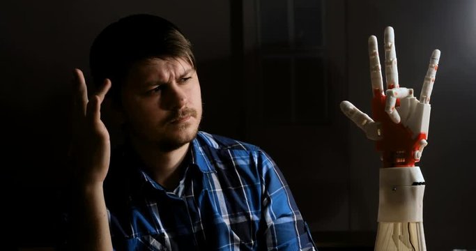 Man creates movement for mechanical plastic arm. Cybernetic robotic arm. Robots arm movement. Futuristic made on 3D printer device.