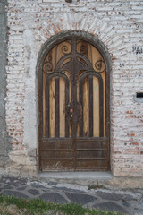 Fototapeta na wymiar An old beautiful ornate arched door, with a white washed brick wall and brick frame work around the arched door, and a stone walkway, in San Miguel de Allende